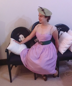 Woman sitting on couch wearing lilac home-made dress. 